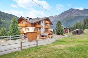 A multi-story wooden chalet with balconies, set against a mountainous backdrop.