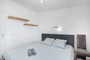 Un dormitorio con una cama, dos estantes en la pared, una lámpara de noche y una silla.