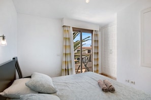 Un dormitorio con cama, almohadas, vistas a un patio exterior con mesa y sillas, y una puerta corrediza de vidrio.
