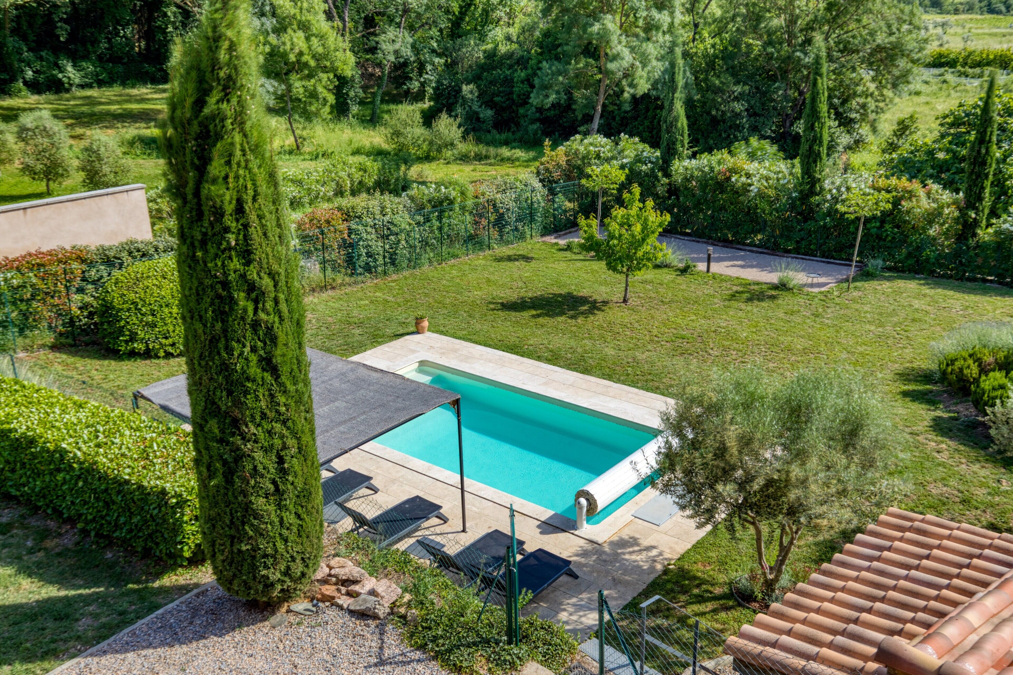 A swimming pool with a tiled deck, surrounded by a well-maintained garden with various shrubs and trees.