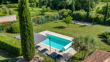 A swimming pool with a tiled deck, surrounded by a well-maintained garden with various shrubs and trees.