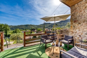 Una terrazza con mobili da esterno, un tavolo con una caraffa e vista su colline verdi.