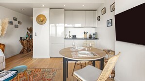 Eine moderne Küche mit weißen Schränken, einem Esstisch mit Stühlen und einem großen Flachbildfernseher an der Wand.