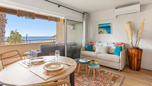 Ein Balkon mit Meerblick, ein Esstisch gedeckt mit Tellern und Gläsern, eine Couch mit Kissen und eine Holzvase mit getrockneten Pflanzen.