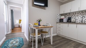 Een compacte keuken met een eethoek, een flatscreen televisie boven de aanrecht en uitzicht op de aangrenzende slaapkamer.