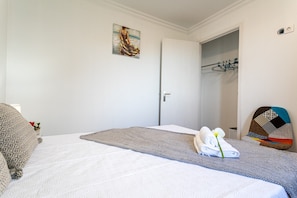 A hotel room with a bed, a painting, a door, and a coat rack.