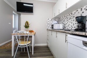 A modern kitchen with white cabinets, a tiled backsplash, a flat-screen TV, and a dining area with a table and chairs.