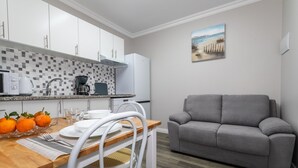 Een compact keuken met witte kastjes, een koffiezetapparaat en een eettafel gedekt met borden, glazen en sinaasappels.