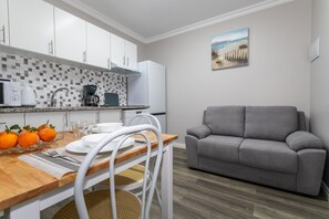 Une cuisine compacte avec des meubles blancs, une machine à café et une table à manger dressée avec des assiettes, des verres et des oranges.