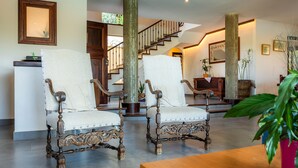 A spacious living area with two ornate chairs, a wooden staircase, and a large potted plant. - Country House 'Es Pujols' with Private Pool, Private Terrace and Wi-Fi (Artá)