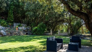 A patio area with outdoor furniture, a stone wall, and a large tree providing shade. - Country House 'Es Pujols' with Private Pool, Private Terrace and Wi-Fi (Artá)