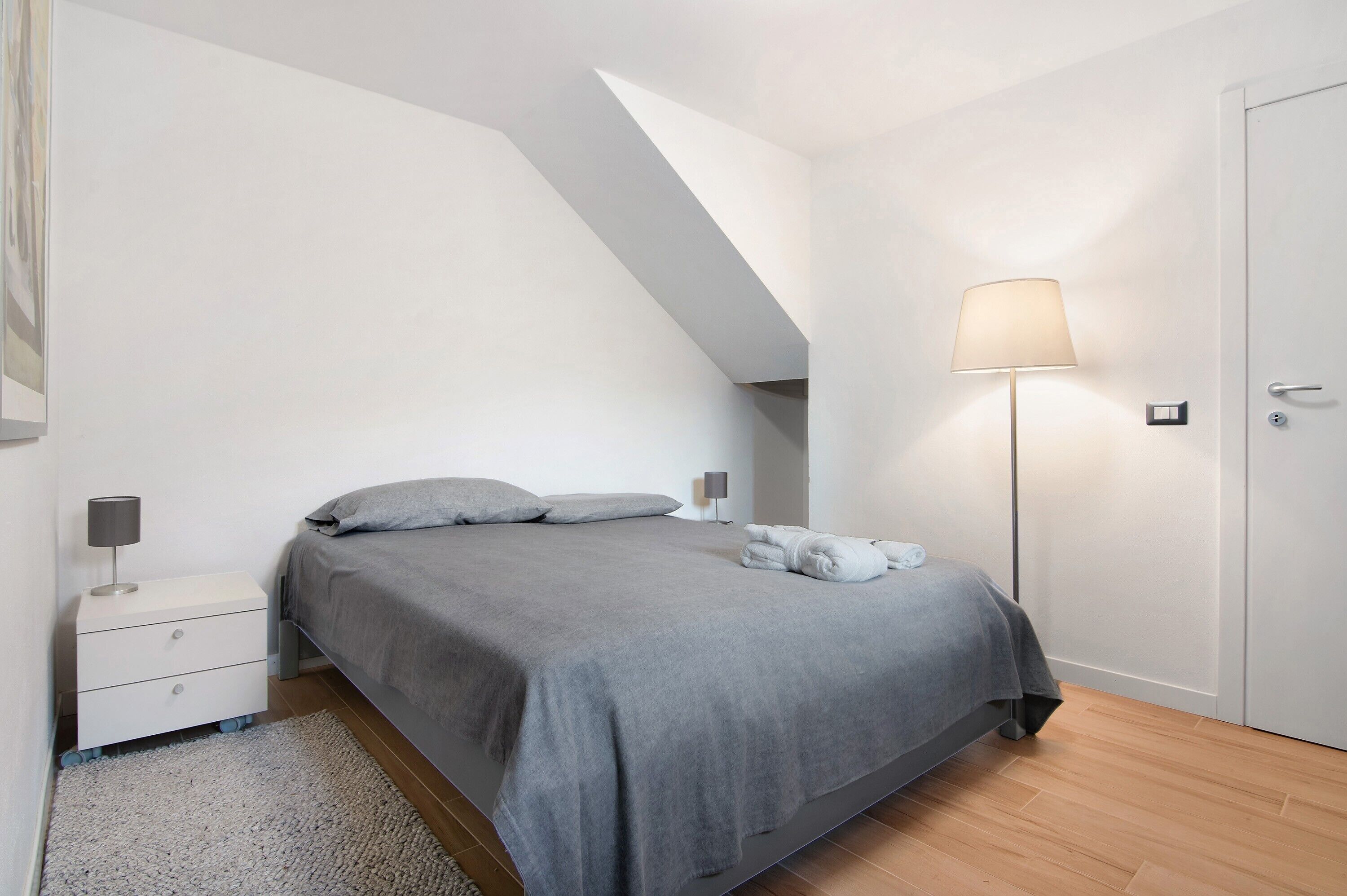 Un dormitorio con cama, mesita de noche, lámpara y una puerta.