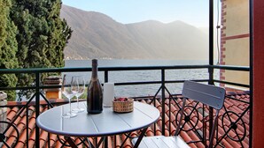 A balcony with a table, two wine glasses, a bottle, and a basket. - Apartment 'Fogazzaro Lake View' with Lake View, Wi-Fi and Air Conditioning (Albogasio-Oria Valsolda)