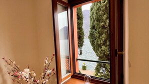 A room with a window overlooking a body of water, a vase with branches, and a candle on the windowsill. - Apartment 'Fogazzaro Lake View' with Lake View, Wi-Fi and Air Conditioning (Albogasio-Oria Valsolda)
