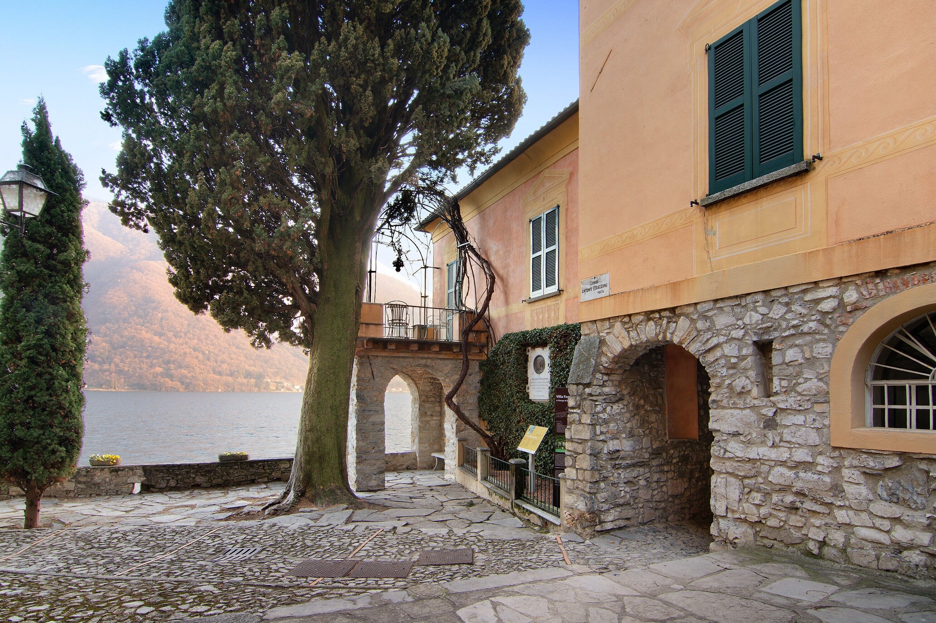 Un edificio in pietra con un balcone, un albero e vista su un lago.