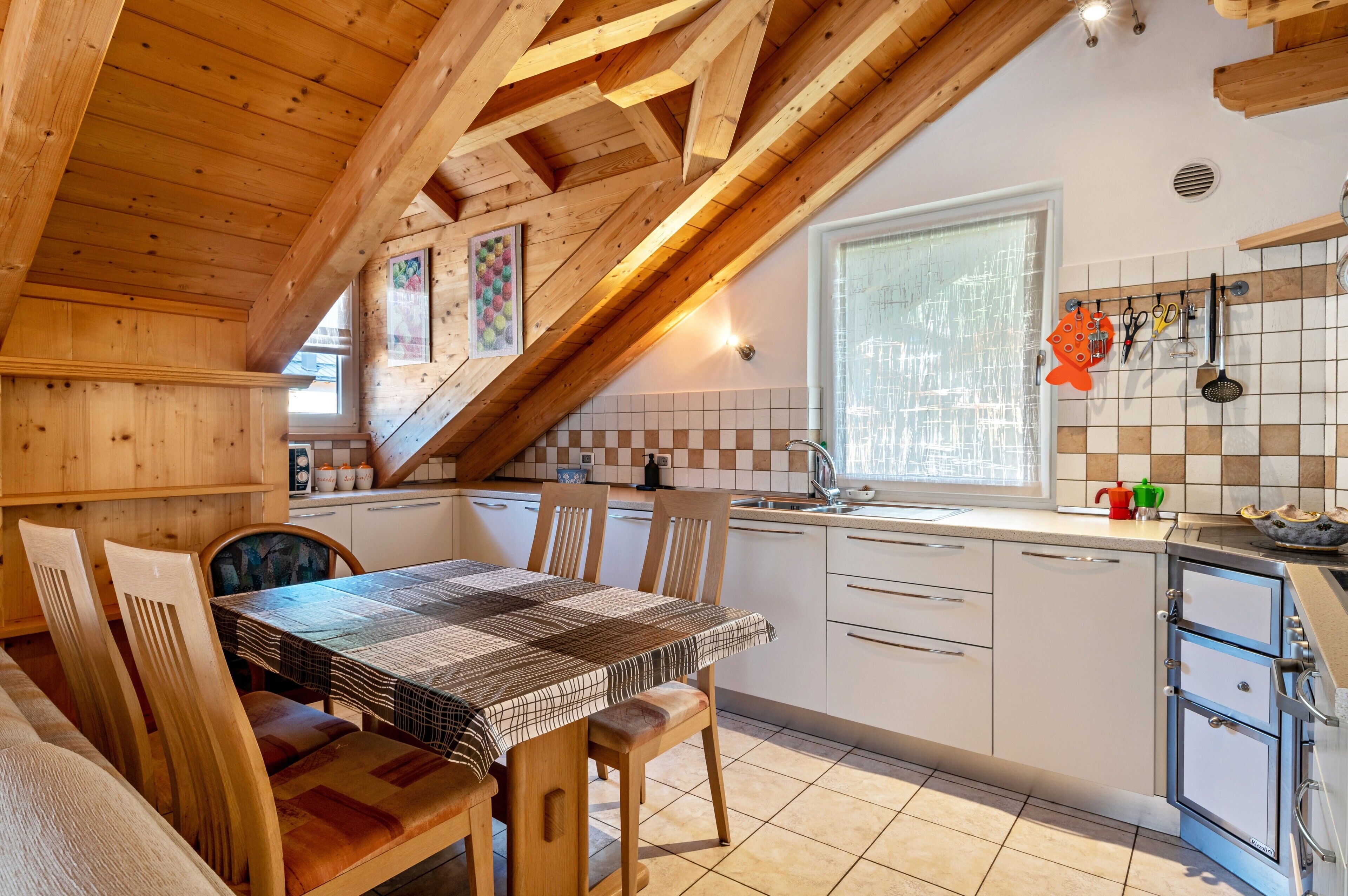 Een keuken met houten balken, een eettafel met stoelen, een raam en een betegelde achterwand.