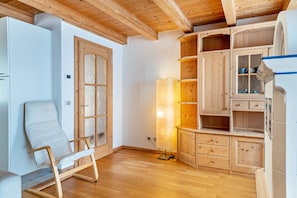 A room with wooden flooring, a white chair, wooden cabinets, and a large window. - Apartment 'Davide ' with Mountain View, Private Garden and Wi-Fi (Pera di fassa)