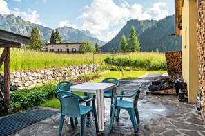 A stone patio with a table and chairs, a stone wall, and a view of mountains. - Apartment 'Davide ' with Mountain View, Private Garden and Wi-Fi (Pera di fassa)