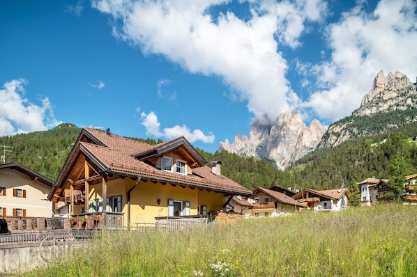 A mountain village with traditional wooden houses, a clear sky, and a prominent rocky mountain in the background. - Apartment 'Davide ' with Mountain View, Private Garden and Wi-Fi (Pera di fassa)