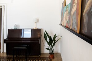 A piano, a lamp, a potted plant, and framed artwork on a wall.