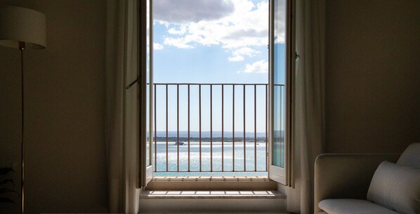 Una habitación con vistas al mar a través de una ventana con barandilla metálica. Se observa un sofá y una mesa con un plato encima.