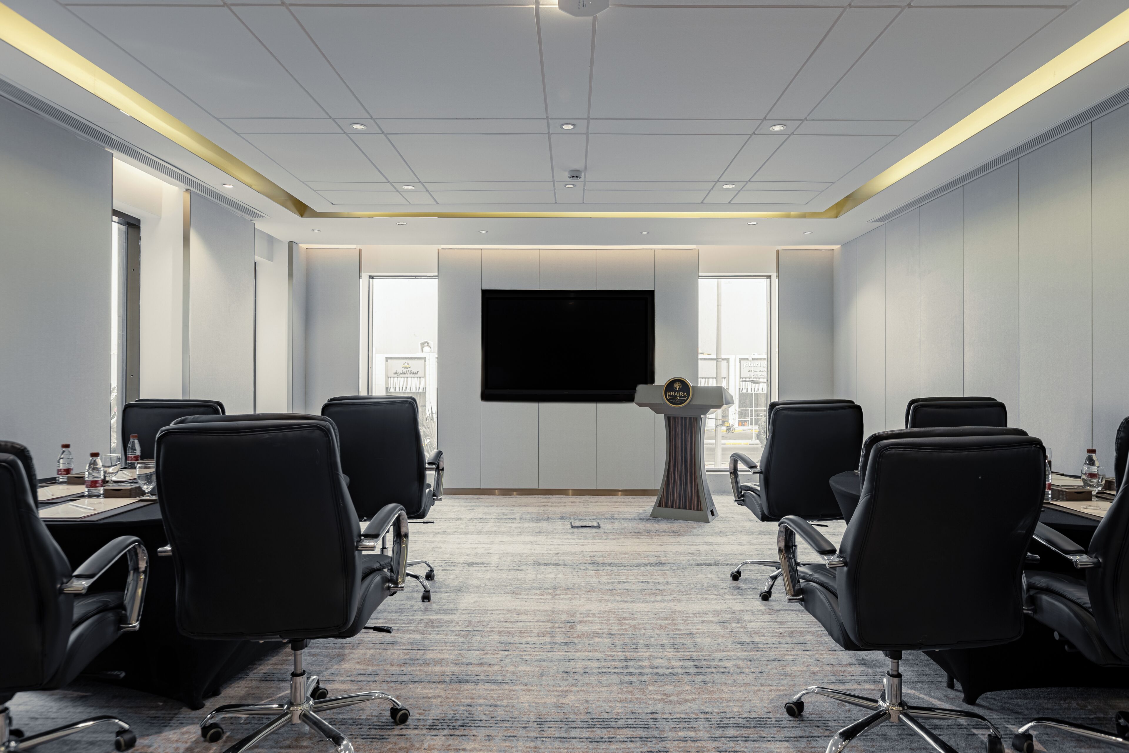A conference room with a large screen, black chairs, a podium, and a carpeted floor.