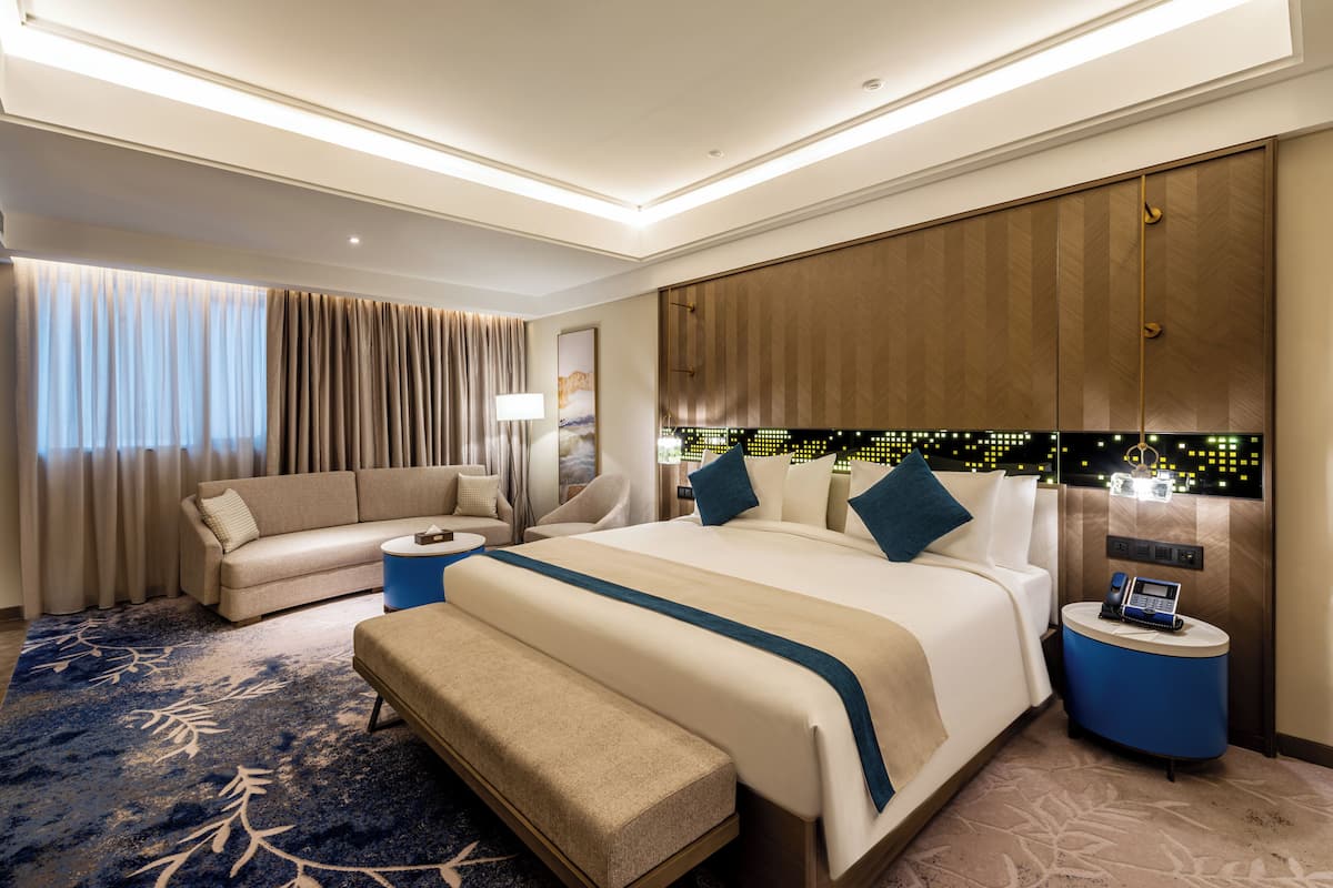 Una habitación de hotel moderna con una cama grande, un sofá, un banco, una mesita y un teléfono en la pared.