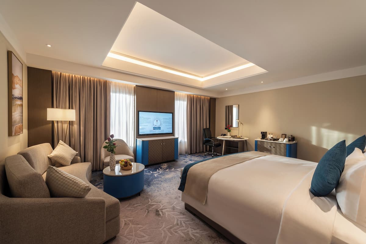 Habitación de hotel con una cama grande, un sofá, un escritorio y una televisión.