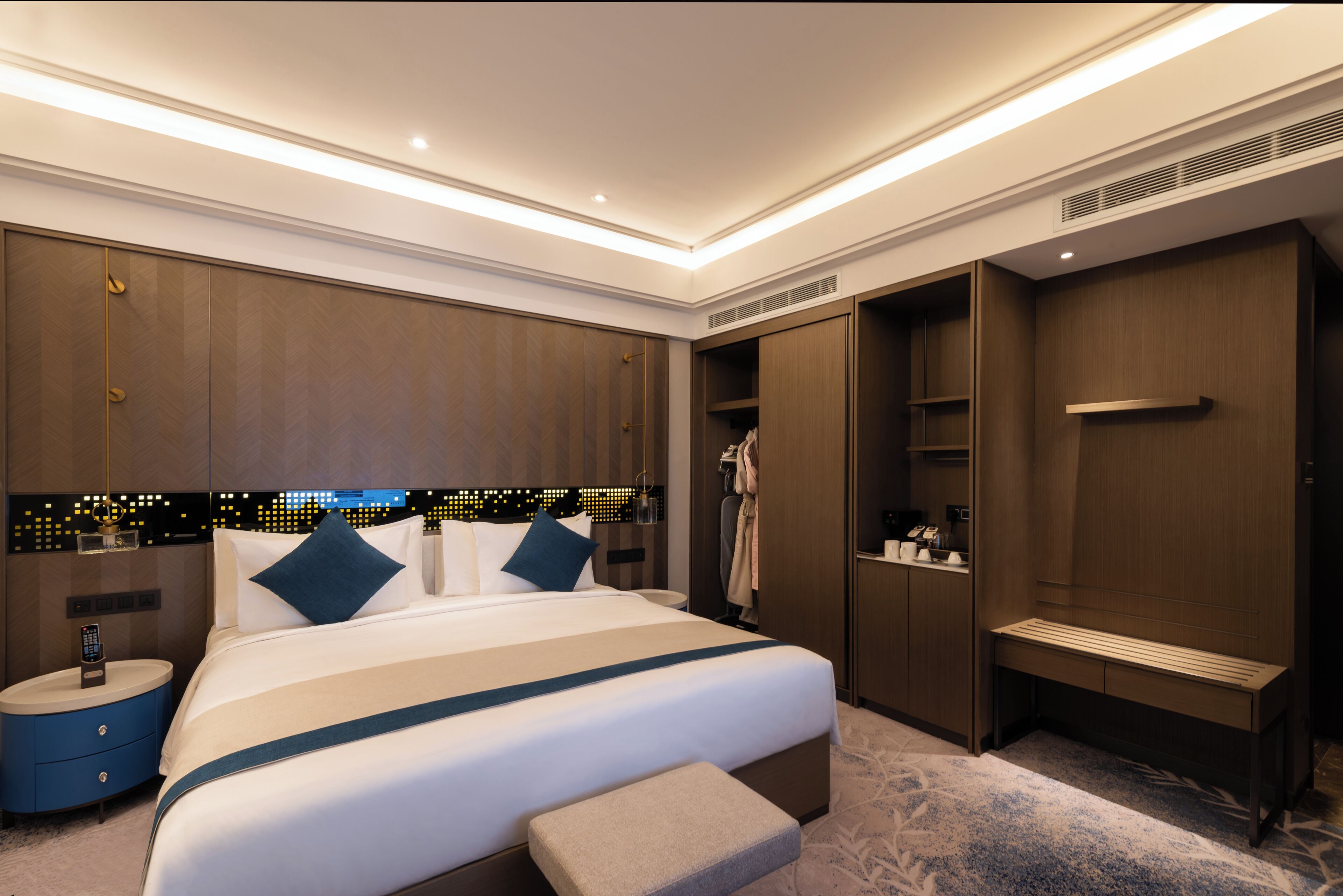Une chambre d’hôtel moderne dotée d’un grand lit, de tables de chevet, d’un banc, d’un dressing et offrant une vue sur le paysage urbain.