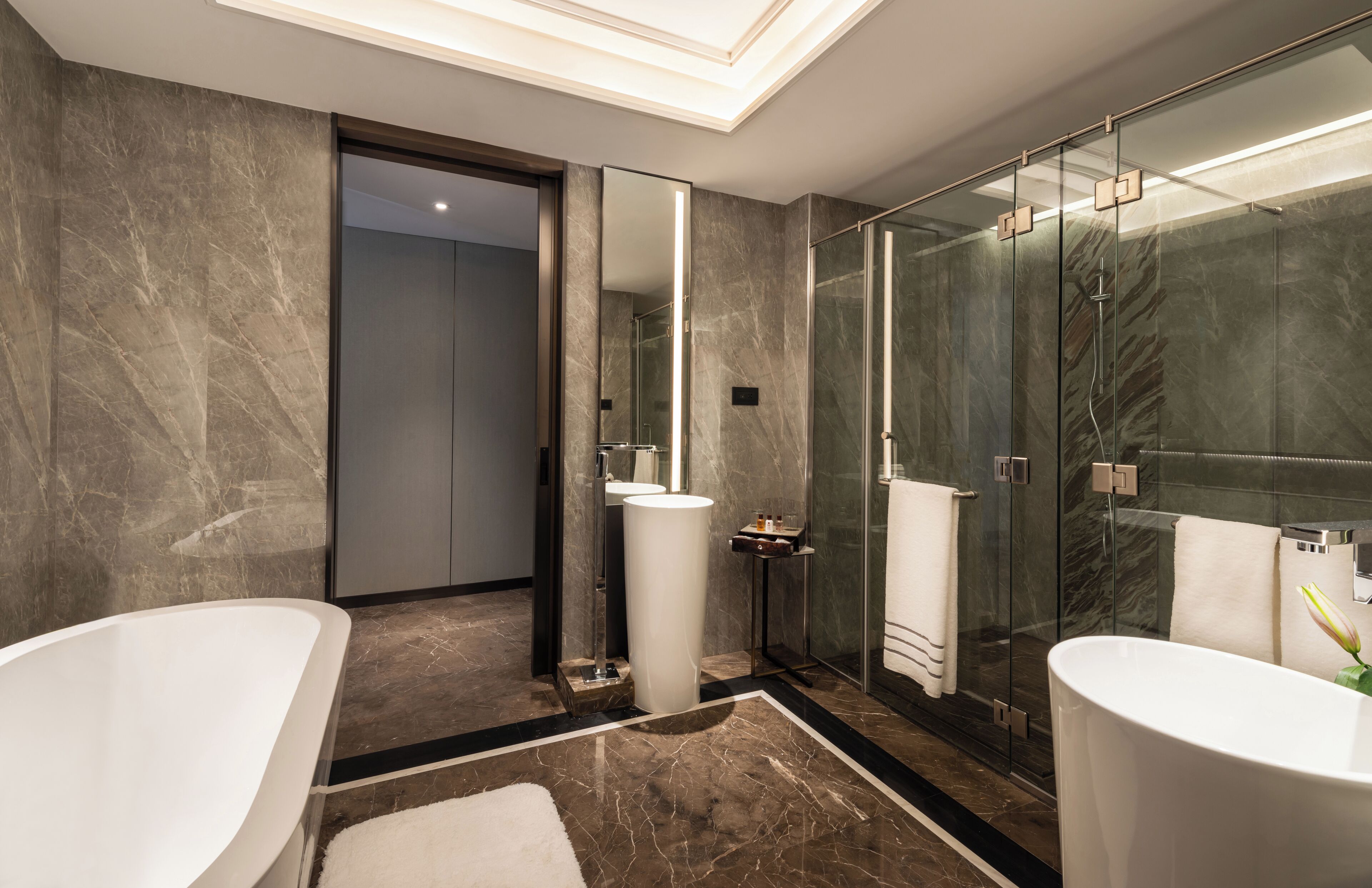 A modern bathroom with two freestanding tubs, a glass-enclosed shower, and a marble floor.