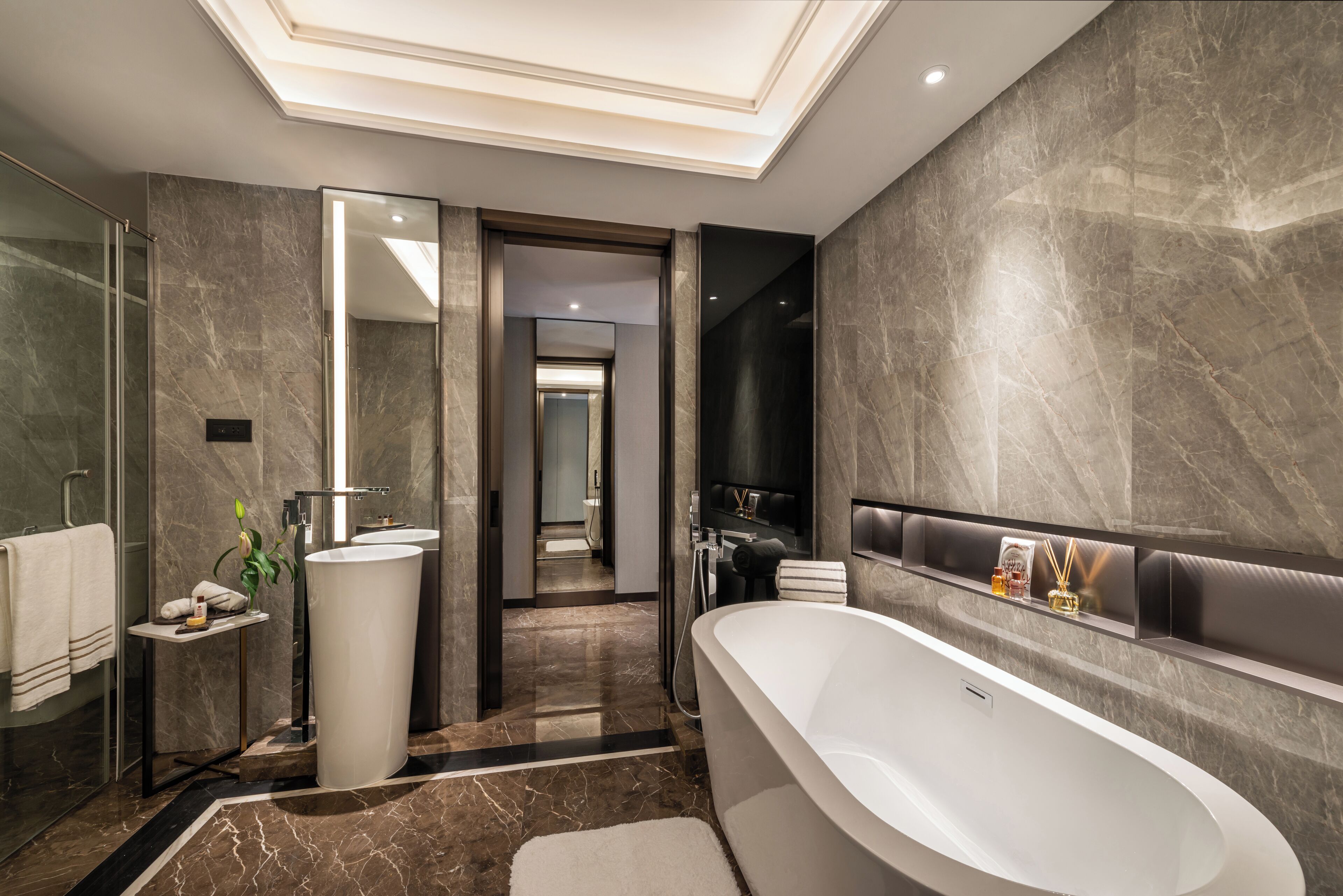 A modern bathroom with a large bathtub, marble walls, and a glass shower enclosure.