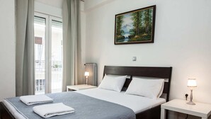 Ein Hotelzimmer mit einem großen Bett, einem Nachttisch mit Lampe, einem Waldgemälde an der Wand und Blick auf den Balkon.