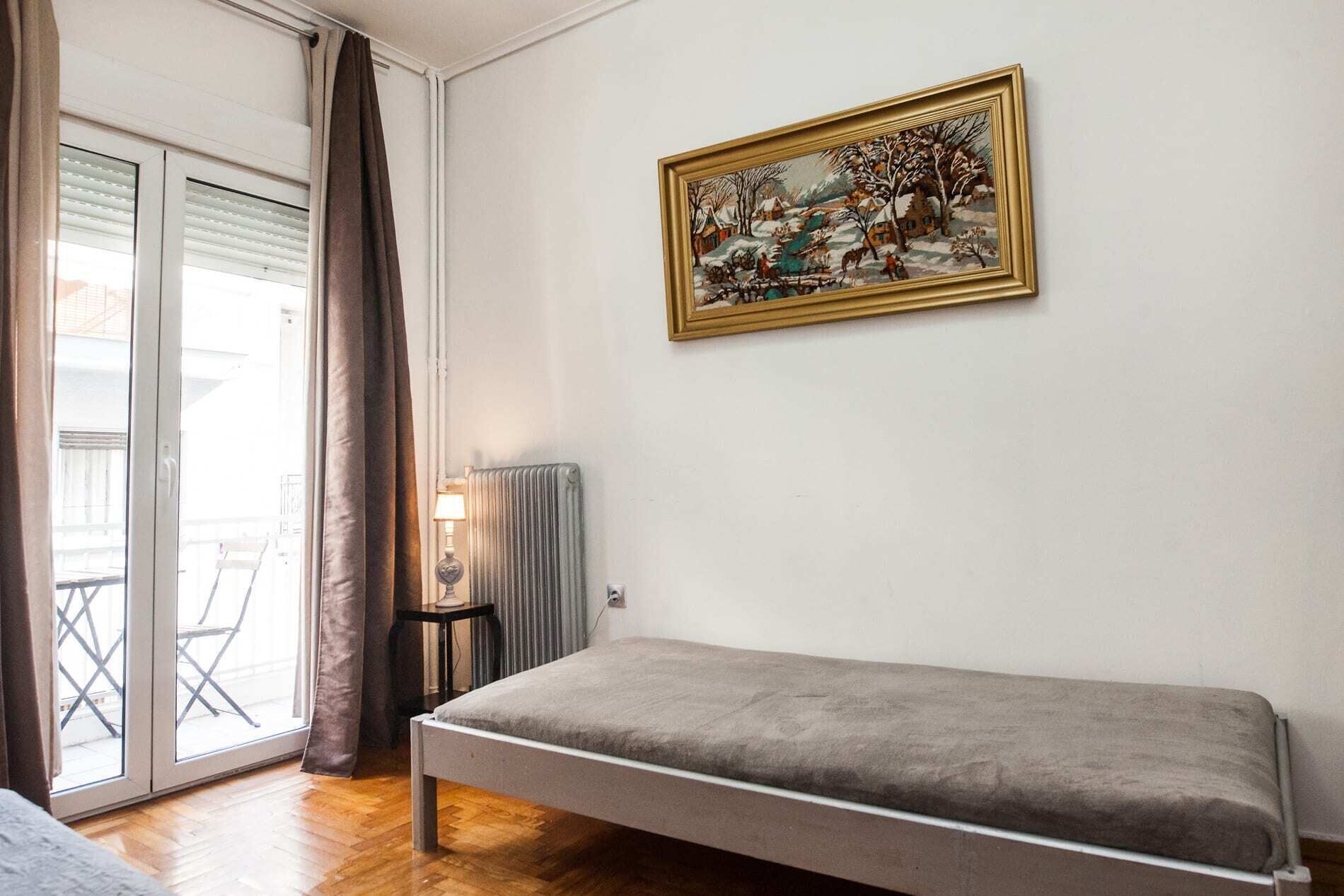 Et soveværelse med seng, radiator, lampe og et billede på væggen.