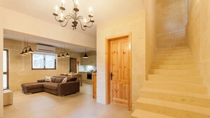 A spacious living area with a sectional sofa, a staircase, and a kitchen in the background. - Naduri, Beautiful Gozitan Villa + Pool (Nadur)