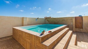 A hot tub with wooden steps and a clear blue pool, surrounded by a stone wall and wooden deck. - Naduri, Beautiful Gozitan Villa + Pool (Nadur)