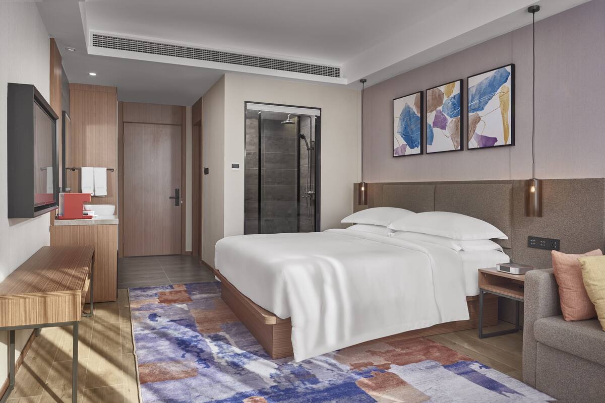 A modern hotel room with a large bed, a desk, a shower, and a sofa.