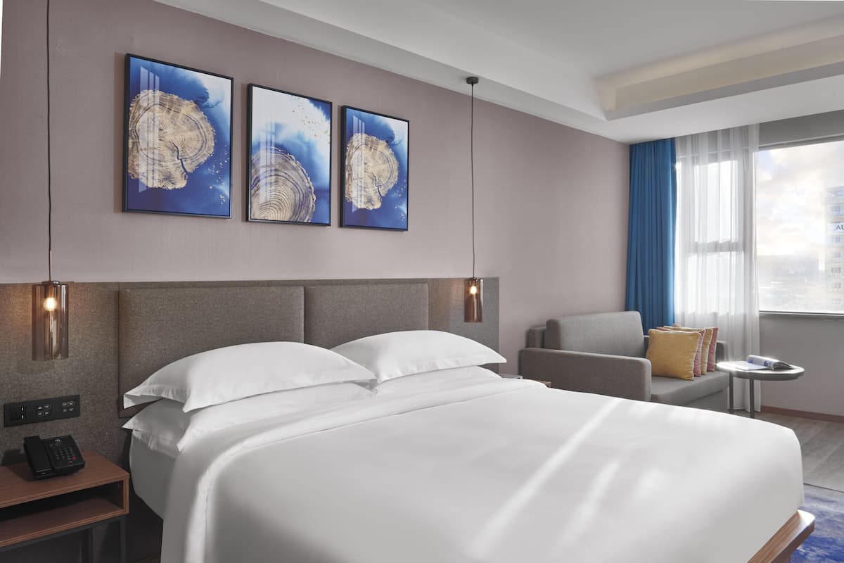 A hotel room with a large bed, a desk with a phone, a chair, and artwork on the wall.