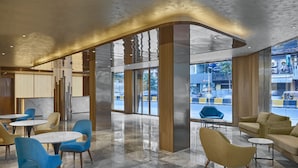 A modern lobby with round tables and chairs, large windows, and a view of the street outside. - Aurea Central Hotel (Phnom Penh)