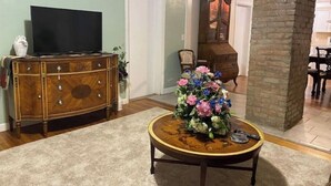 A living room with a wooden cabinet, a television, a floral centerpiece on a round table, and a brick pillar.