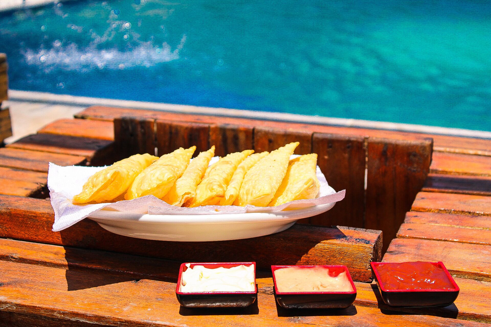 Un plato de pasteles dorados sobre una mesa de madera junto a una piscina.