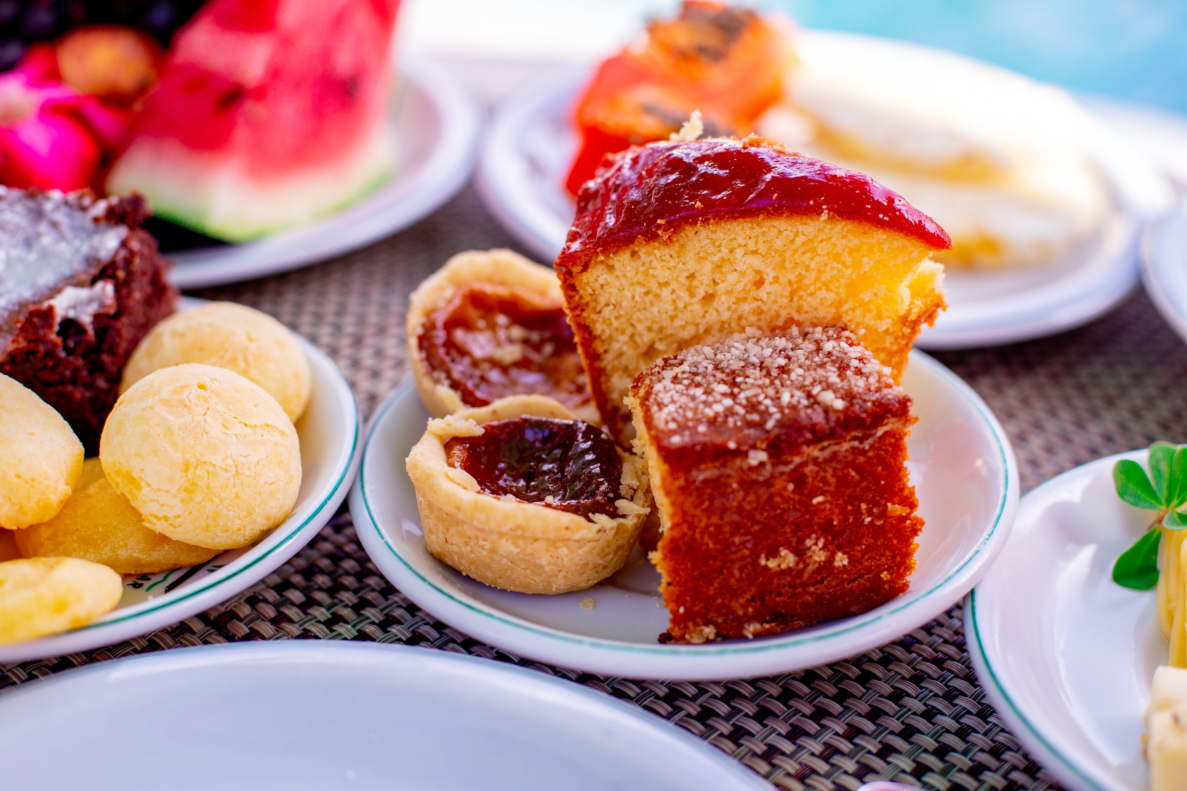 A variety of desserts on plates, including a slice of cake with a red topping and a small tart with a dark filling.