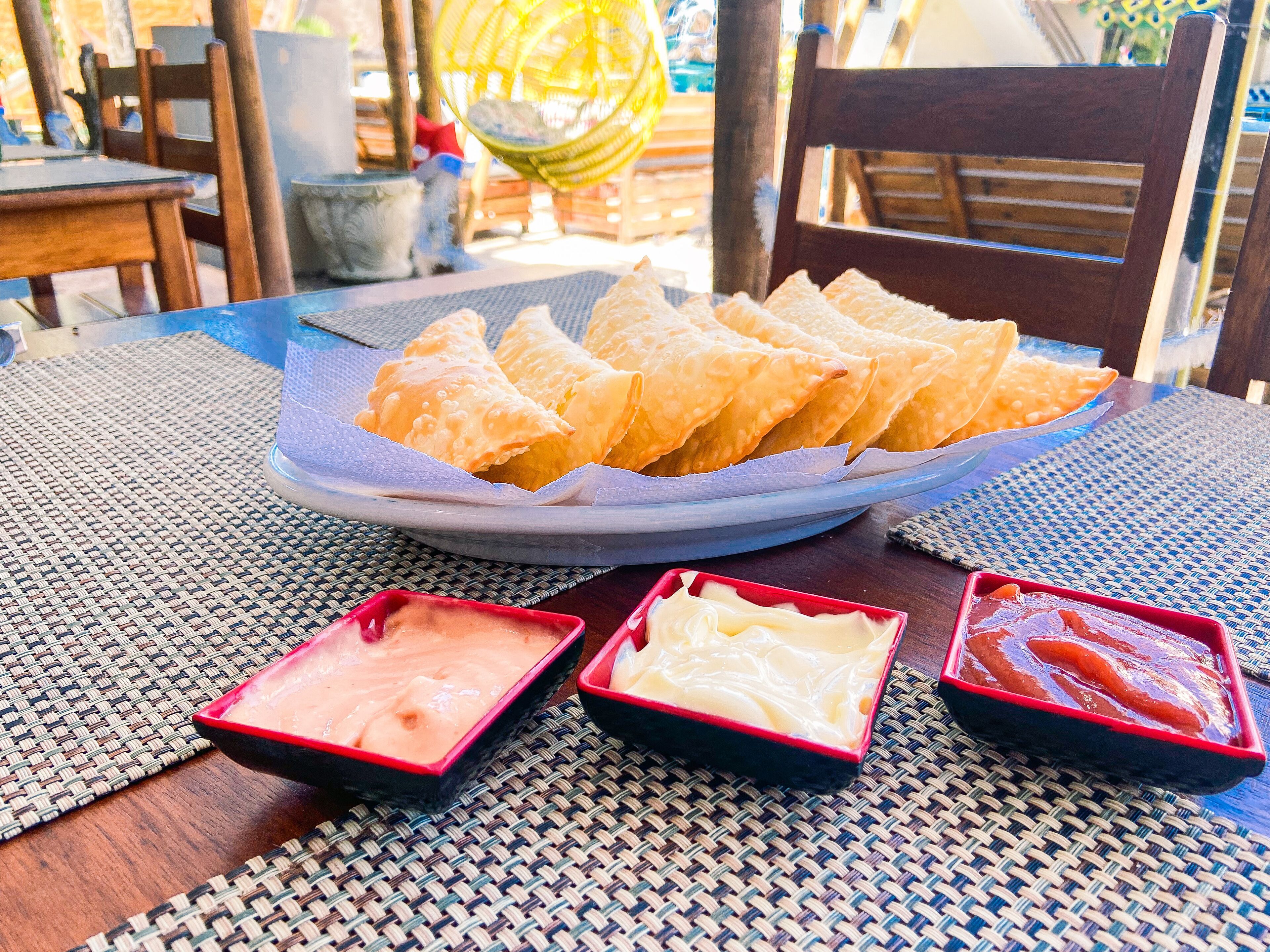 A plate of fried snacks with three dipping sauces on a woven table mat.