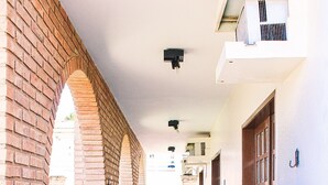 Un espacio al aire libre cubierto con pared de ladrillo, banca de madera y planta en maceta con flores rosadas.