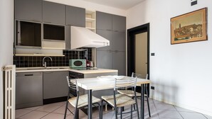 A compact kitchen with grey cabinets, a white countertop, and a dining area with a white table and wicker chairs.