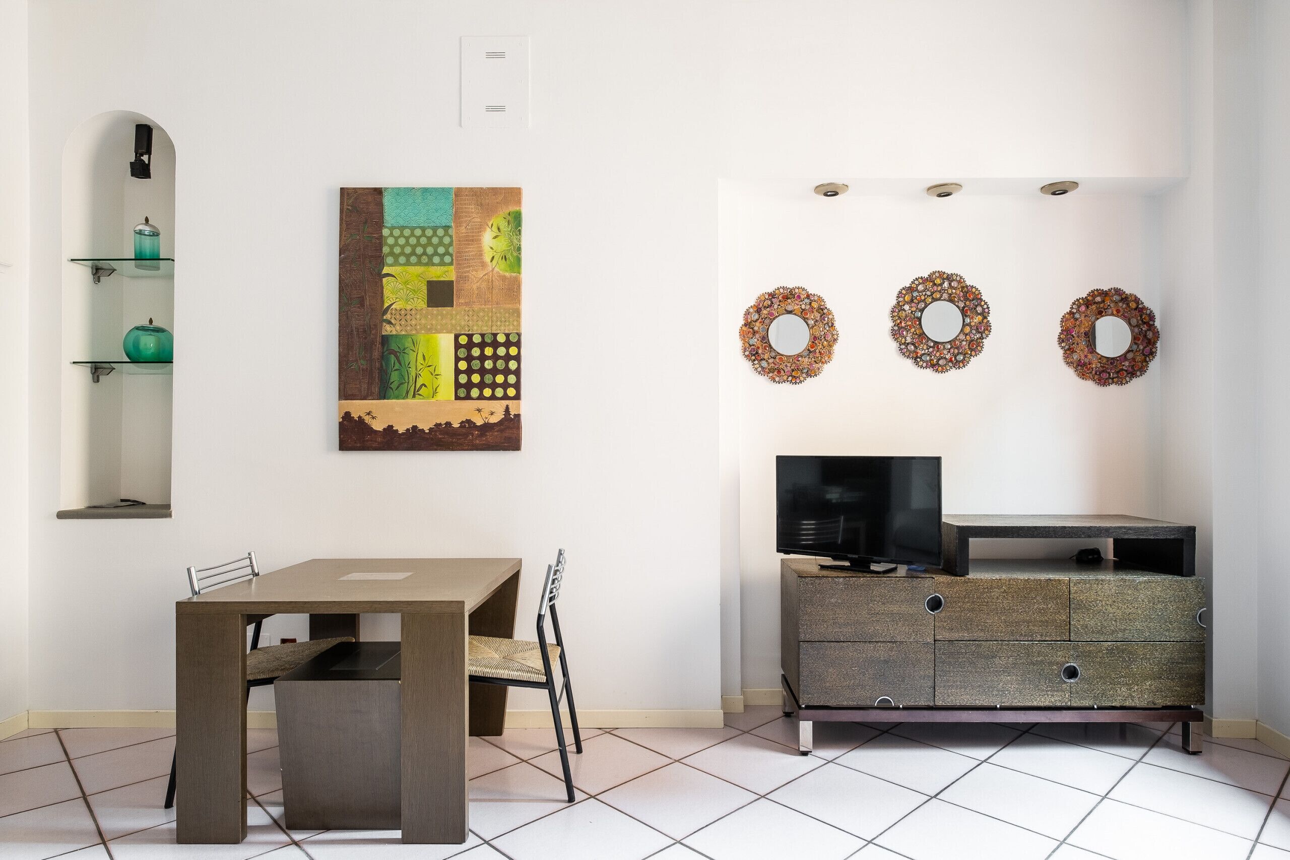 Een eethoek met een tafel en stoelen, een kast met een televisie, en decoratieve wandkunst.