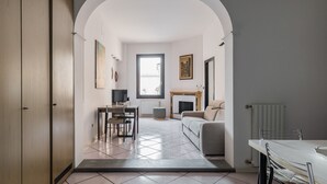 A modern living room with a fireplace, a dining area with a table and chairs, and a kitchen visible through an archway.