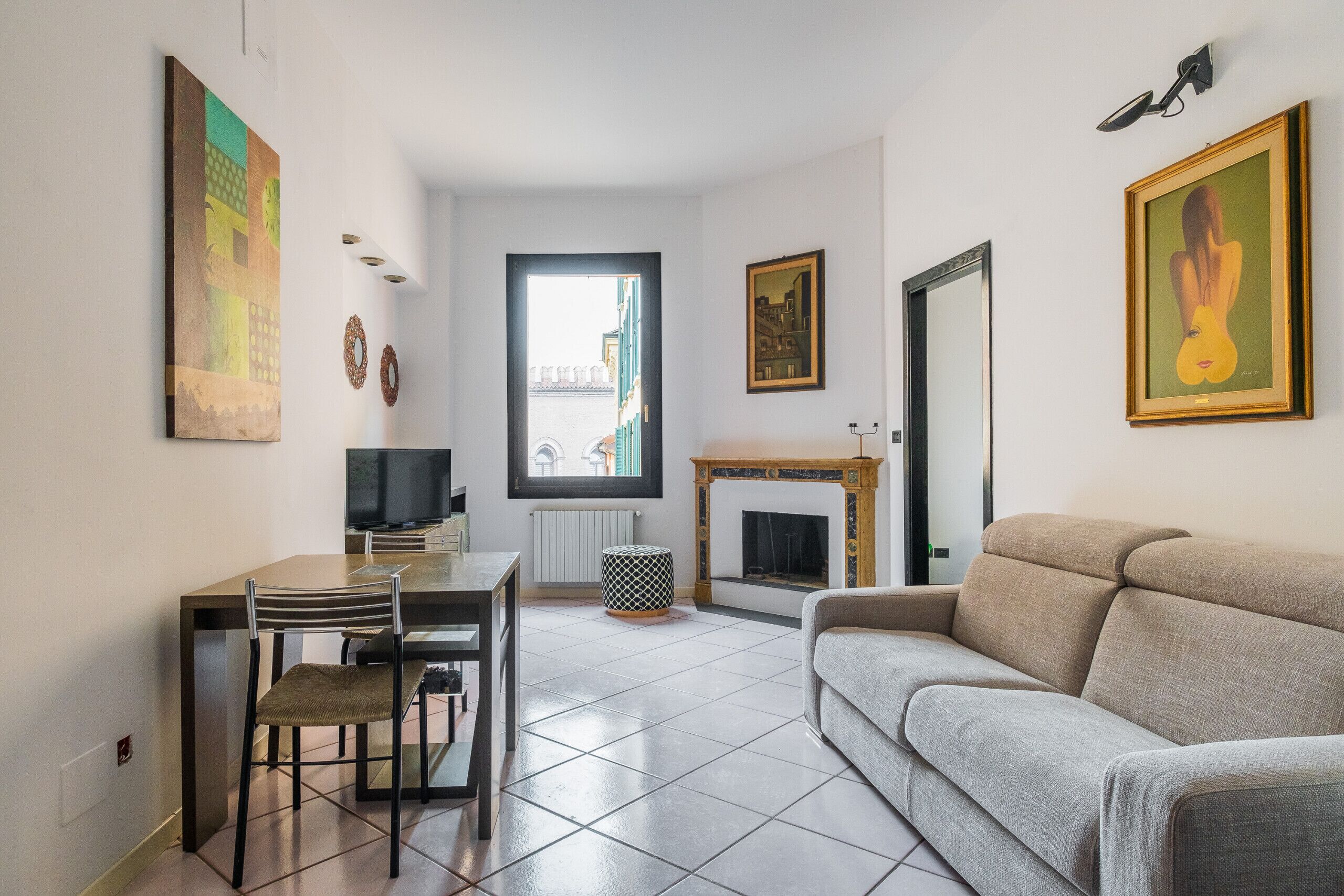 Una sala de estar con un sofá, una mesa de comedor con sillas, una chimenea y obras de arte en las paredes.
