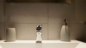 A modern bathroom with a white sink, two cylindrical soap dispensers, and a unique faucet design.