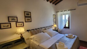 A bedroom with a bed, bedside lamps, a window with curtains, and framed pictures on the wall. - Tenuta Colombaio  (Casole d'Elsa)