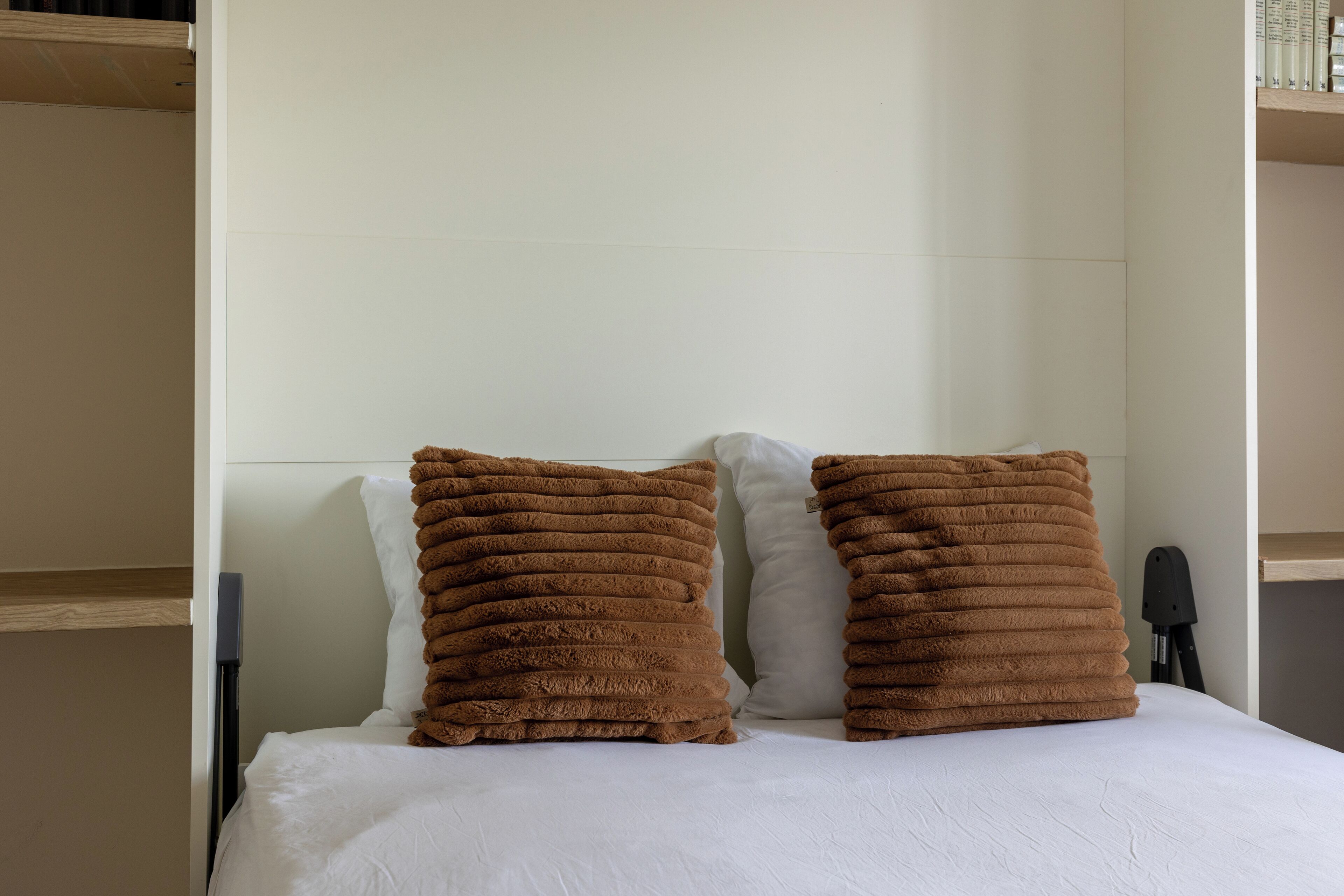 A bed with white bedding and two brown pillows.